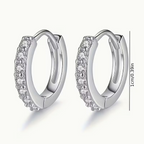 Lumière Pavé Huggie Hoop Earrings – silver huggie hoops on wooden surface with white flower